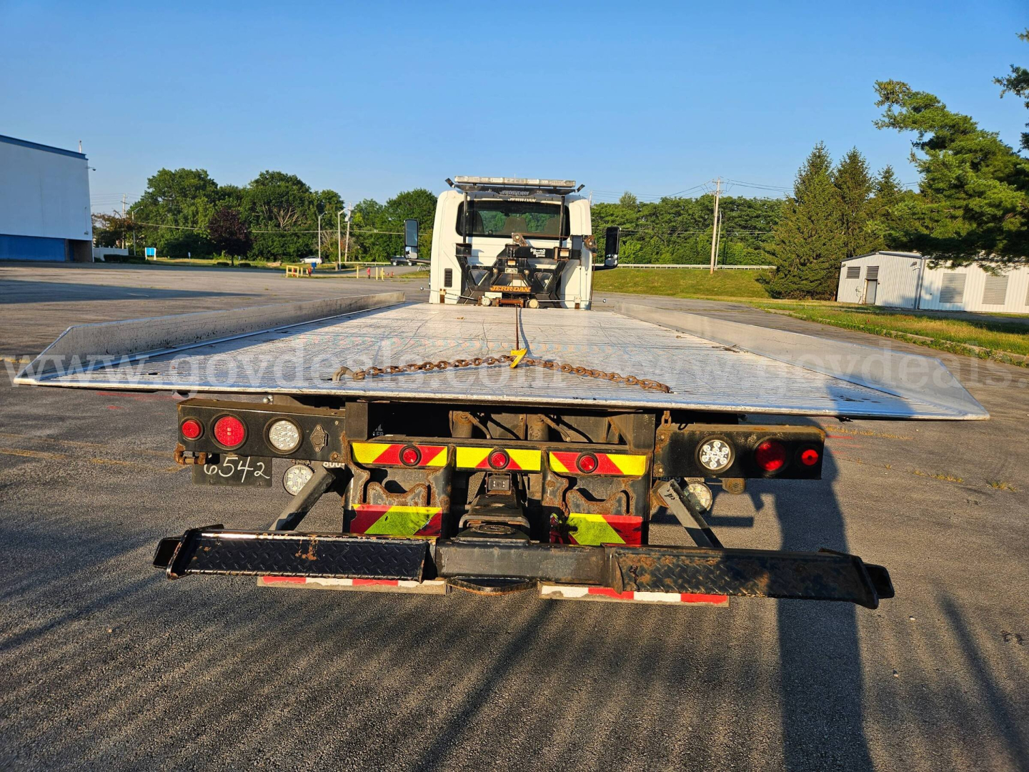 Flatbed tow truck deck with rear view showing trailer with reflective chevrons and taillights.