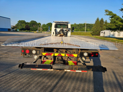 Flatbed tow truck deck with rear view showing trailer with reflective chevrons and taillights.