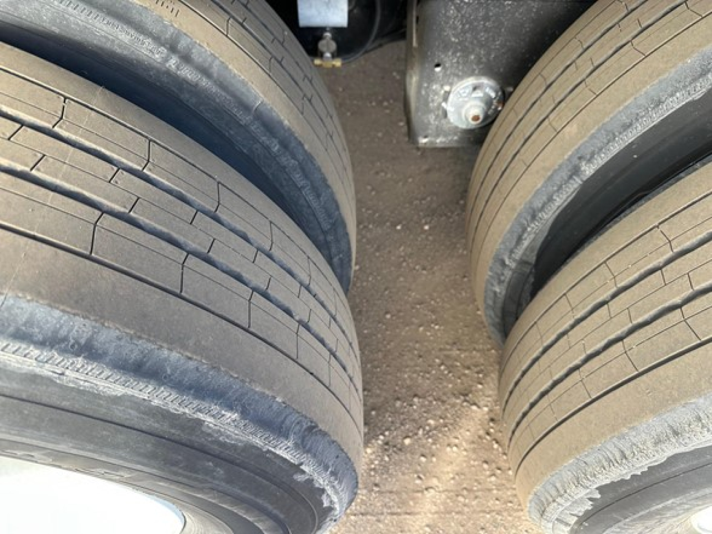 Two pairs of truck trailer tires on a 2026 Manac flatbed trailer showing dual axle tires and clean asphalt surface between wheels.