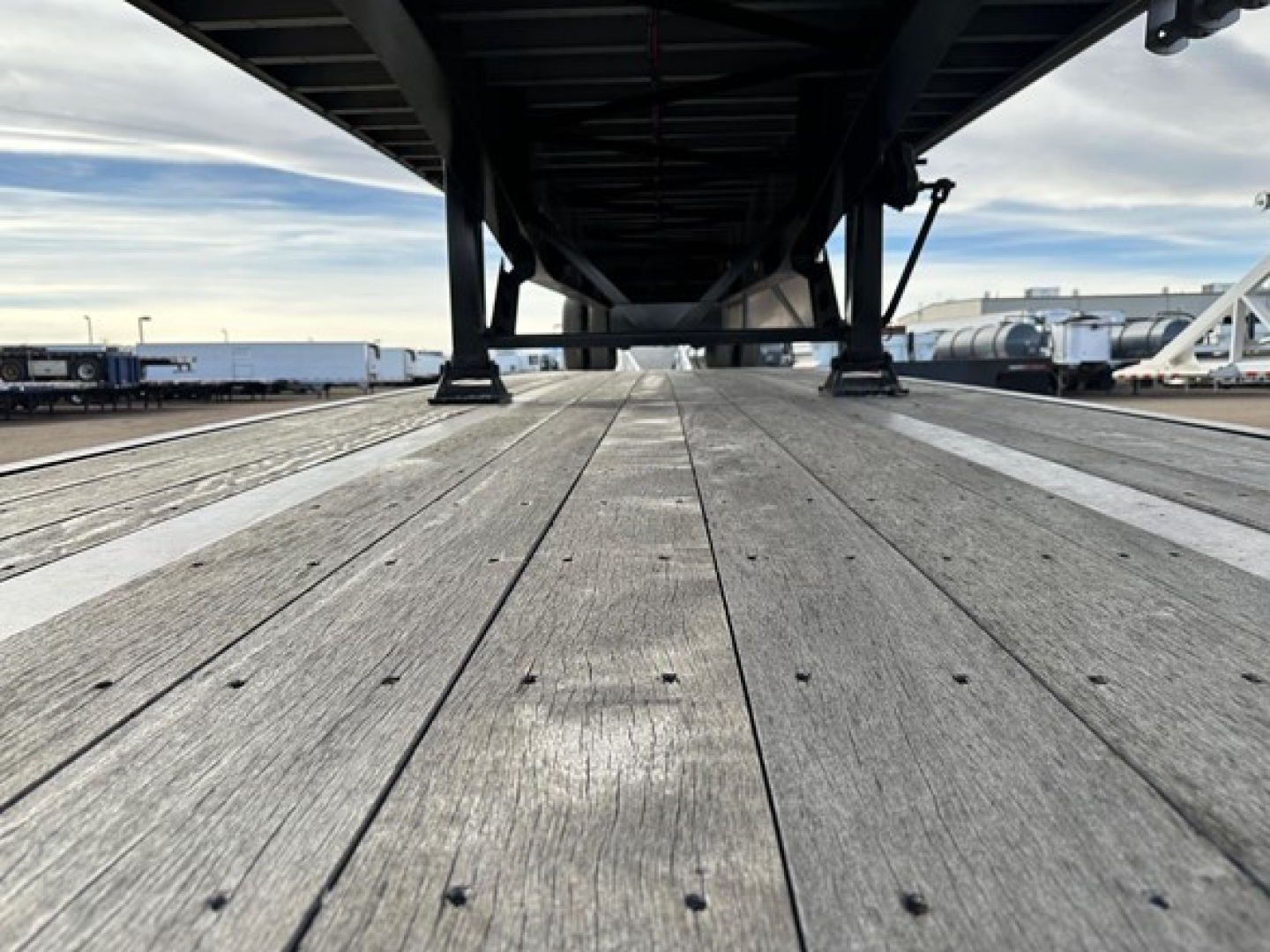 Flatbed trailer deck viewed from ground level under the frame showing wooden planks and support beams.