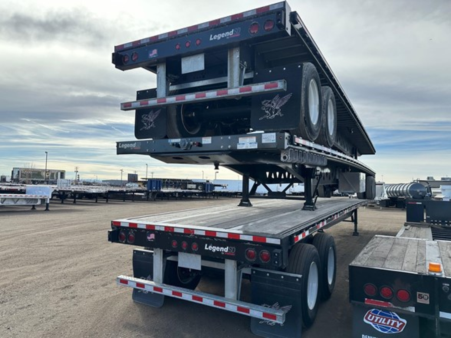 Manac steel 48' flatbed trailer with air ride and air pin slide in retracted position, dual rear axles, stacked on a trailer yard.