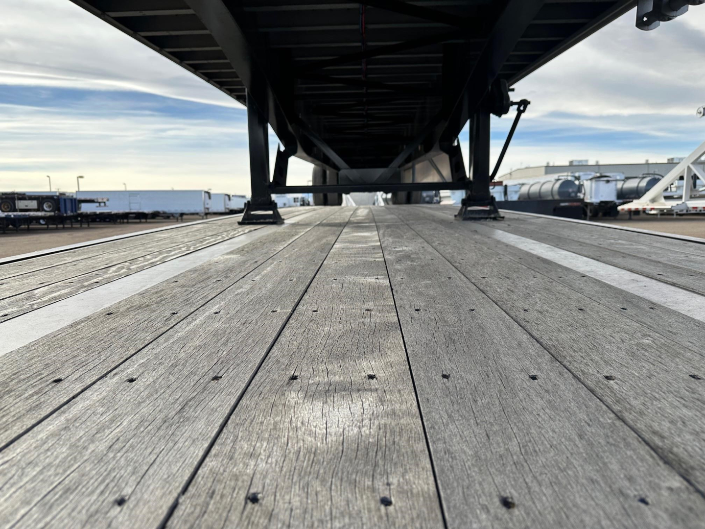 Flatbed trailer deck view from underneath showing wooden planks and undercarriage with metal supports.