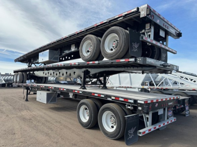Manac 48' flatbed trailer stacked with another trailer on top, dual rear axles visible, black with reflective tape and wheels, outdoor lot.