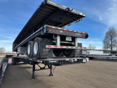 Flatbed trailer in elevated position showing dual rear axles, black metal frame, and Legend-brand branding on the sides. 48' length, trailer on site with support legs deployed.