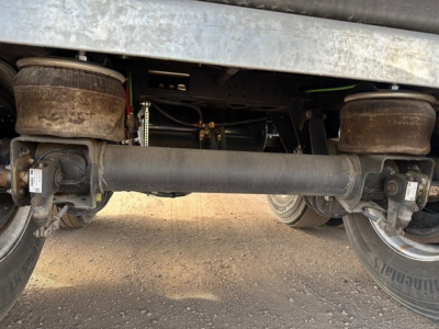 Flatbed trailer undercarriage with air ride suspension and slide mechanism showing axles, air bags, and drive components.