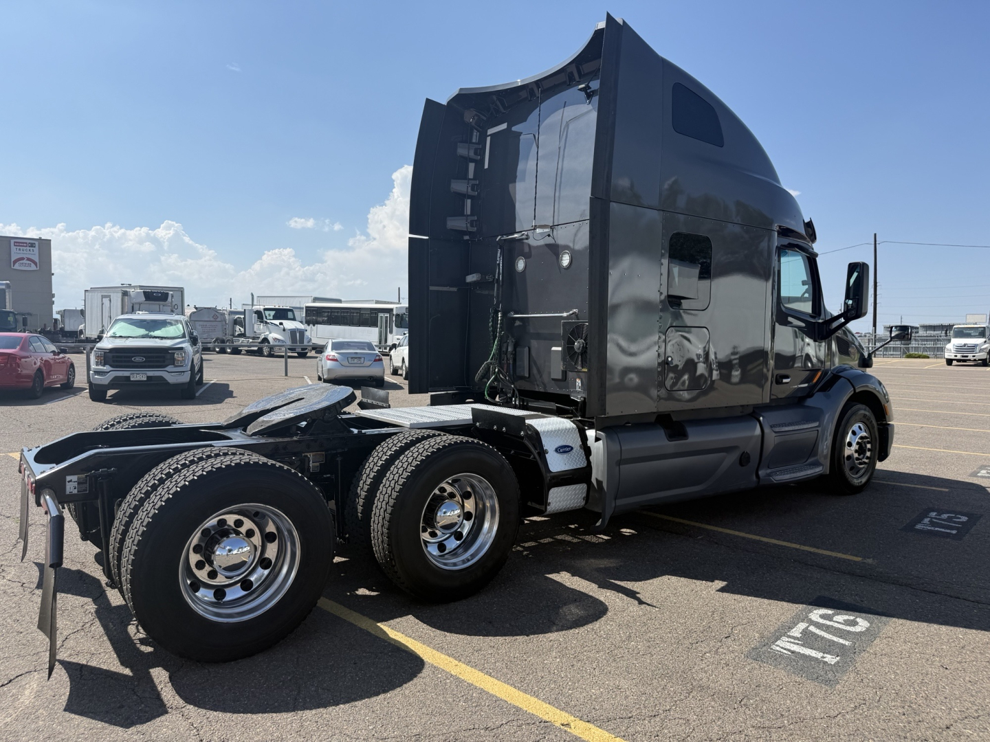 Peterbilt 579 conventional sleeper truck in a parking lot, side view showing rear triple axles and black glossy exterior. Visible text includes VIN plate and numbers on gear, no identifiable logo readable.