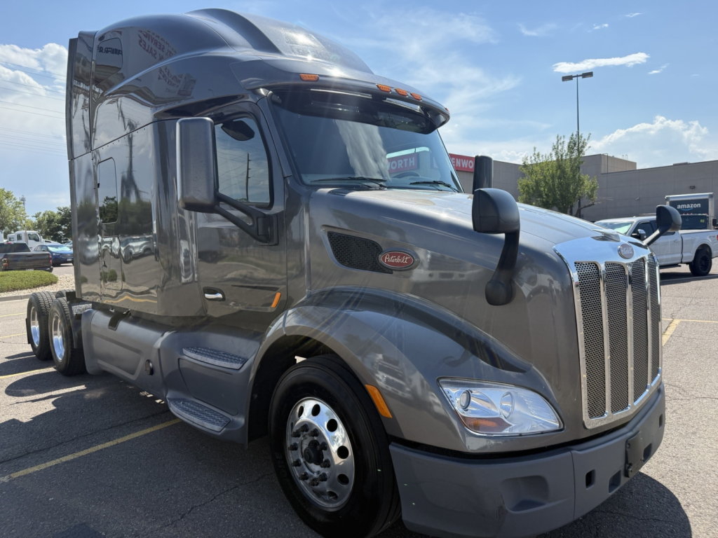 Peterbilt 579 tractor-trailer cab in metallic gray, side view showing aerodynamic sleeper, large grille, dual mirrors, and nav lights.