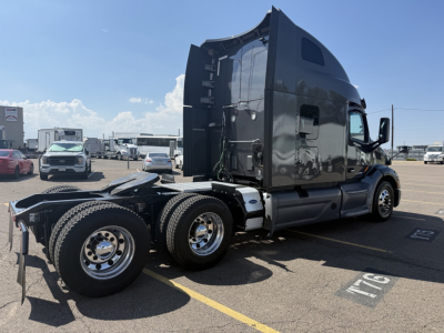 Peterbilt 579 conventional sleeper truck in a parking lot, side view showing rear triple axles and black glossy exterior. Visible text includes VIN plate and numbers on gear, no identifiable logo readable.