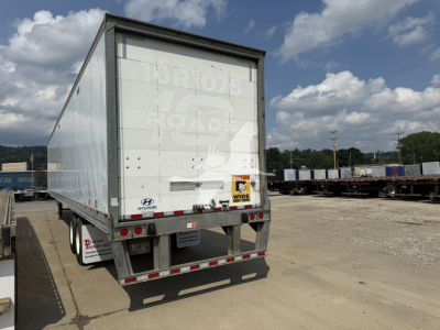 Rear view of a Hyundai roll door trailer with white weathered exterior, showing taillights, bumper, and Hyundai logo; stock trailer yard in background.