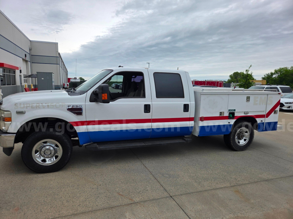 Ford F-250 service/utility truck with emergency vehicle livery, side compartments, large crew cab, dual rear wheels, long bed; white with blue and red stripe; running boards; stock number 558-272.