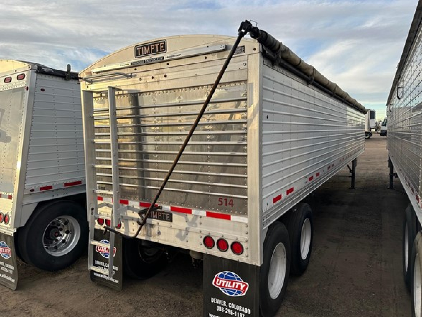 Timpte Super Hopper trailer showing rear end with doors and logo, tandem axles, reflective decal strips, and hydraulic tarp system.