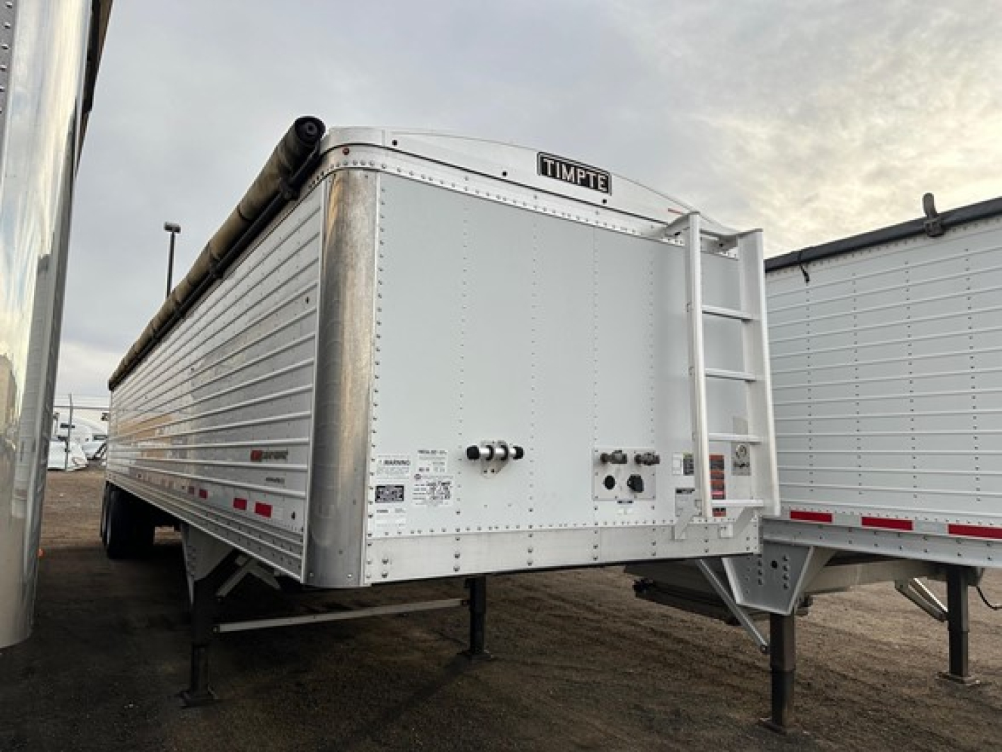 Timpte Super Hopper trailer rear view showing ladder and discharge area with Timpe brand label; metal corrugated side panels and support legs visible.