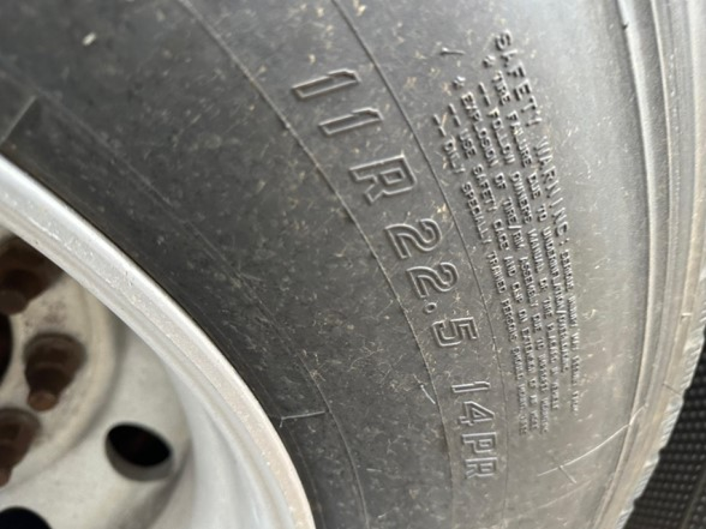 Tire sidewall with embossed numbers and small warning text. Visible: '10 R 22.5 14PR' and a block of vertical small print (stencil) along the inner edge.