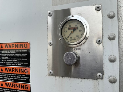 Hopper trailer exterior panel showing a round gauge (0-100) and two warning stickers; metal plate with dump toggle and label; weathered surface