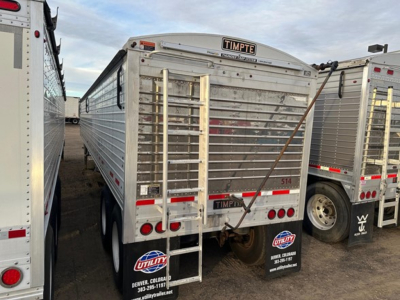 Timpte Super Hopper trailer rear view showing the metal body, ladder, and rear lights. Brand name TIMPTE on top center, two-axle configuration, utility bumper stickers visible.