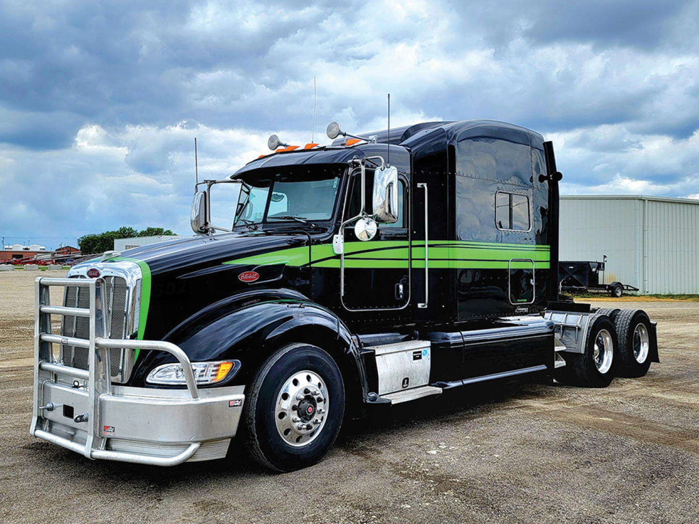 Peterbilt 386 UltraCab tractor in black with green stripe, front chrome bumper, grille guard, and sleeper cab, three axles visible, daytime outdoor lot.