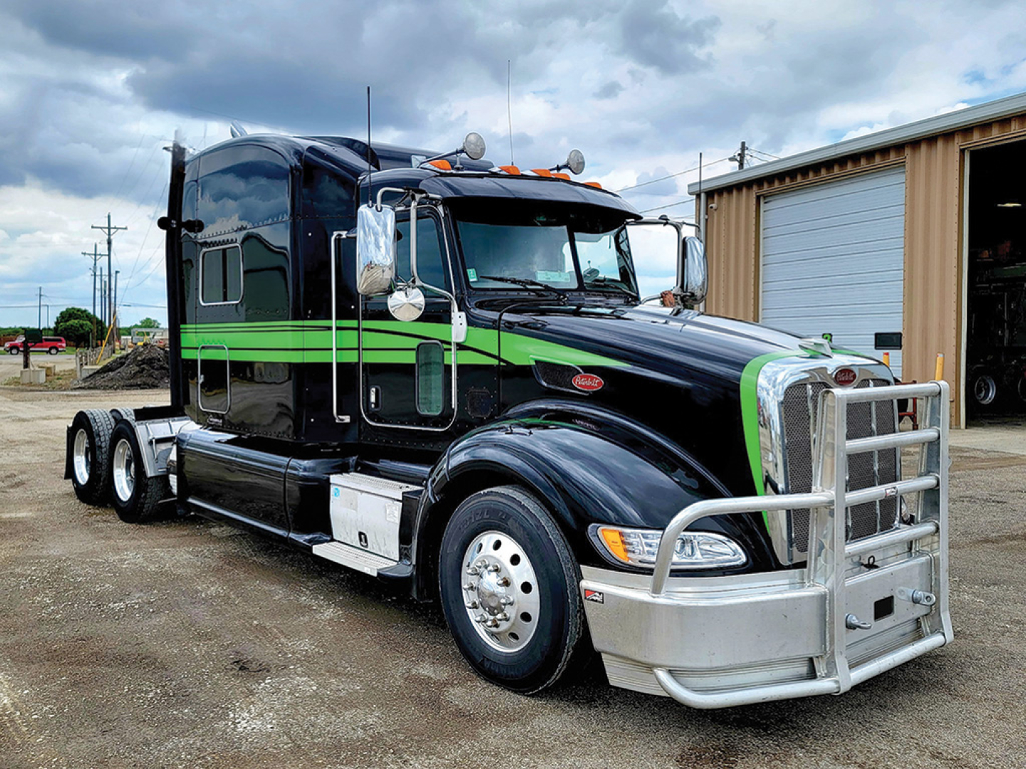 Peterbilt 386 UltraCab tractor in black with green stripe, three-axle configuration, chrome bumper and grille, exterior fuel tanks, side mirrors, and sleeper cab.