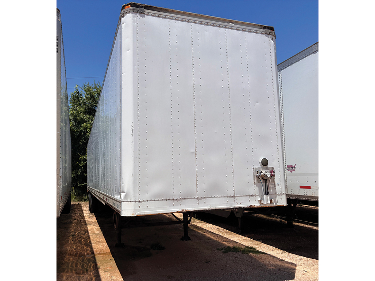 Trailer corner showing white Stoughton aluminum van body with rear swing door and riveted panels.