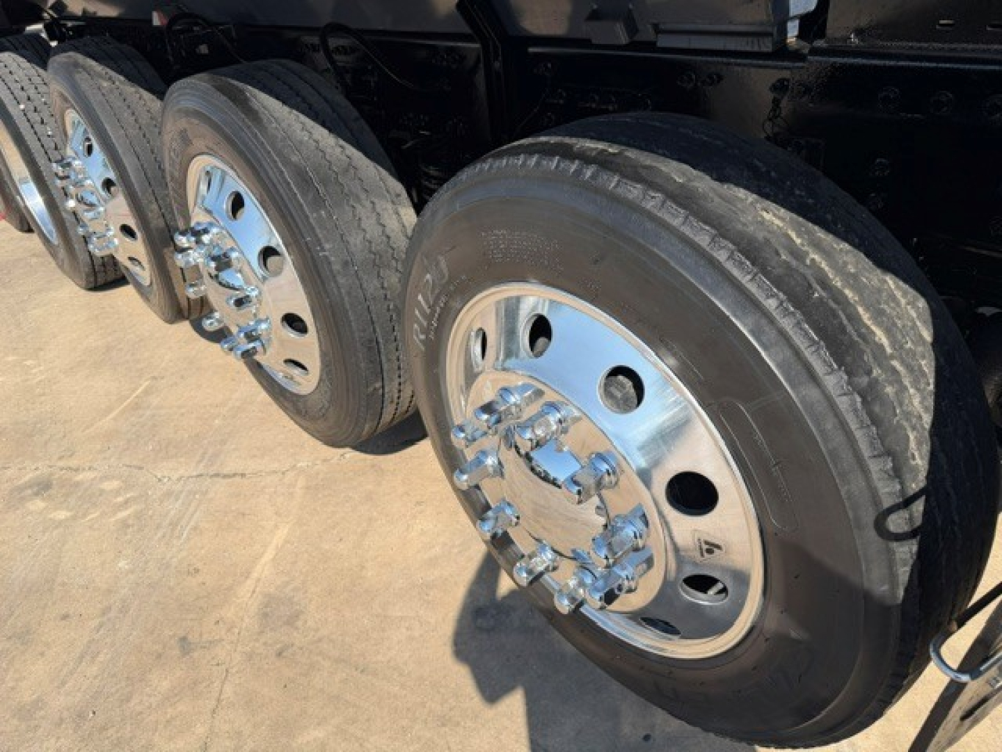 Wheel end of a Volvo truck showing silver chrome wheel hub with multiple lug nuts and tire. Tread and tire sidewall visible.
