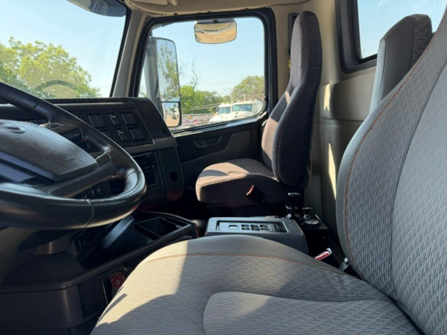 Cab interior of a Volvo VHD truck showing front seats, steering wheel, and center console. Visible are dashboard controls and driver/passenger seats.