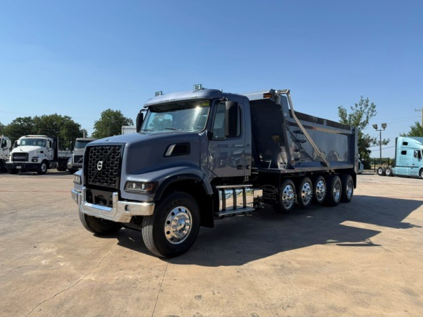 Volvo VHD104F300 dump truck in service showing side of cab and 6-wheel dump trailer with chrome wheels and Volvo emblem.
