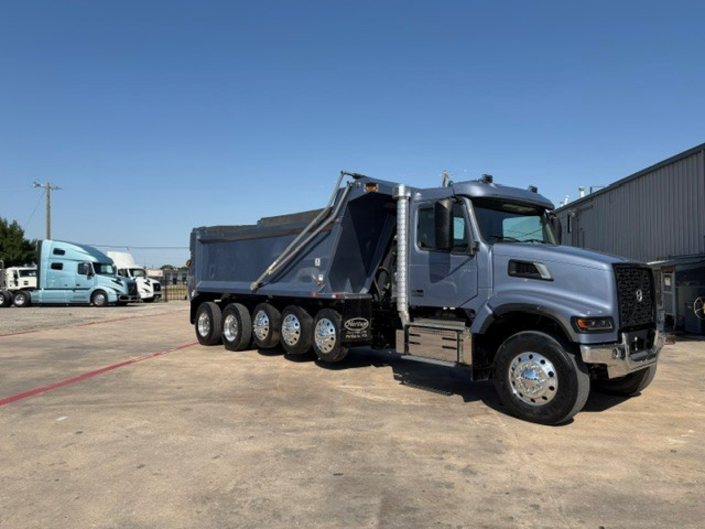 Volvo VHD104F300 dump truck with a blue cab and multiple rear axles, side view showing bed and hydraulic dump mechanism.