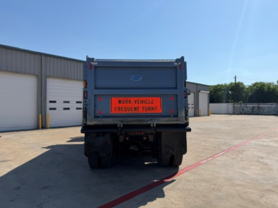 Rear view of a Volvo dump truck showing the tailgate and a bright orange warning sign reading 'WORK VEHICLE FREQUENT TURNS' on the dump bed.
