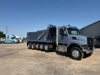 Volvo VHD104F300 dump truck with a blue cab and multiple rear axles, side view showing bed and hydraulic dump mechanism.