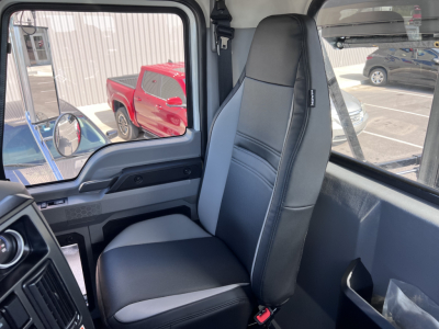 Truck cab interior showing driver seat and window with reflections in a Mack GR64B roll-off truck.