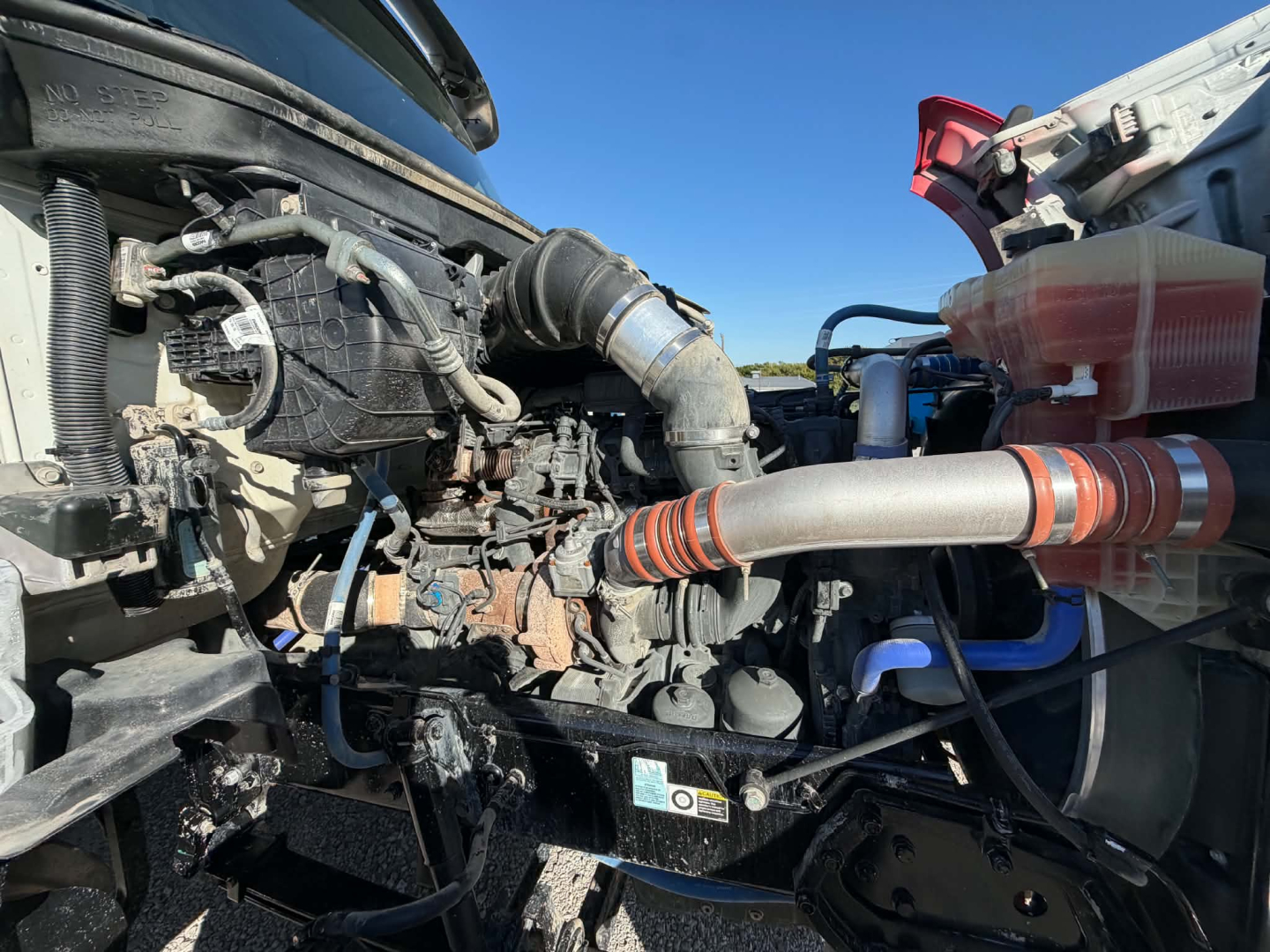 Kenworth T880 engine bay showing diesel engine components and hoses; view includes air intake, turbo hose, coolant reservoir, and surrounding mechanical fittings.