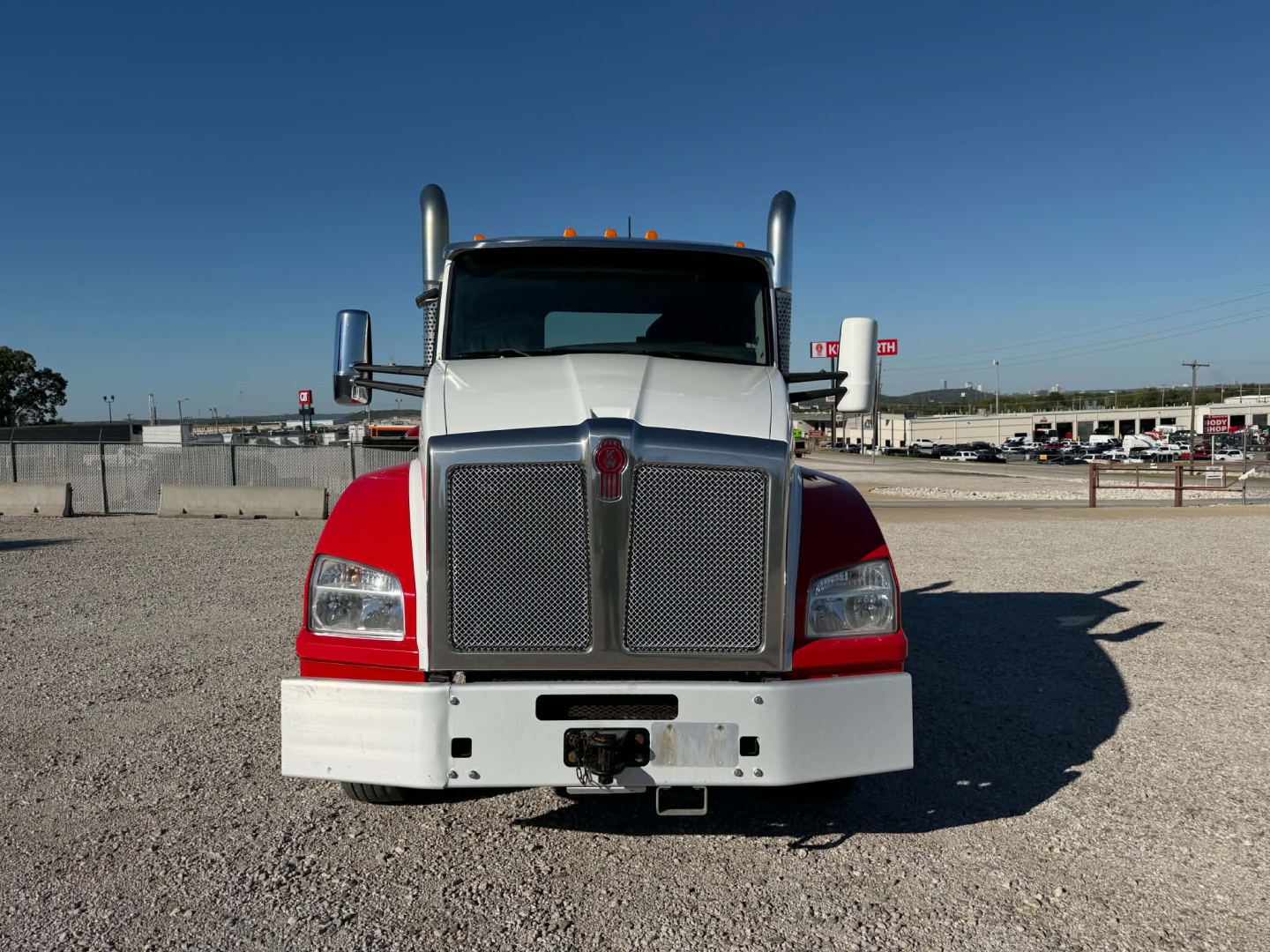 Kenworth T880 conventional daycab front view showing large chrome grille, white bumper, red fenders, dual large mirrors, and vertical exhaust stacks.