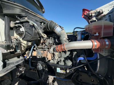 Kenworth T880 engine bay showing diesel engine components and hoses; view includes air intake, turbo hose, coolant reservoir, and surrounding mechanical fittings.