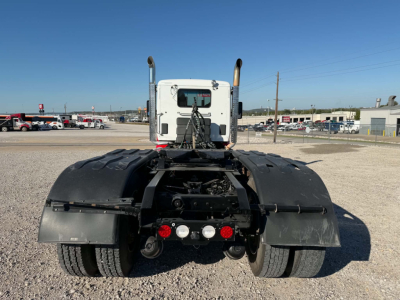 Kenworth T880 rear view showing dual rear wheels, mud flaps, and chassis with fifth wheel and fuel lines visible; rear lights and bumper area intact.