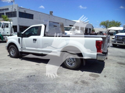 Ford F-250 SD XL pickup truck in a parking lot, side view showing crew cab, long bed, white exterior, utility rack and toolbox in bed.