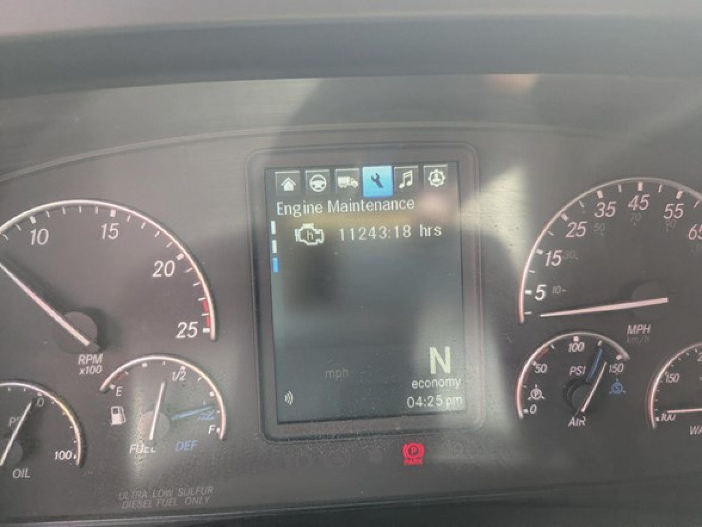 Truck instrument cluster display showing Engine Maintenance with 11243:18 hrs, N gear, economy mode, in-dashboard screen flanked by RPM and speed gauges.