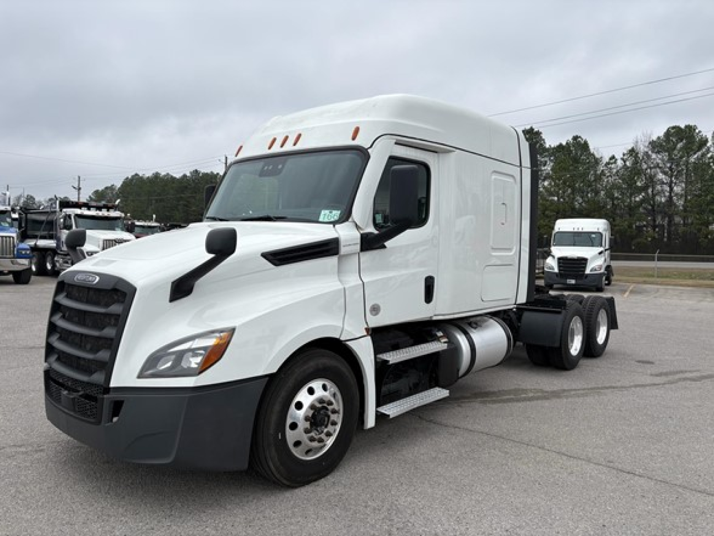 Freightliner Cascadia 126 semi-truck towed in a parking lot, white cab with sleeper, front view showing large grille and side exhaust, no visible sponsor text.