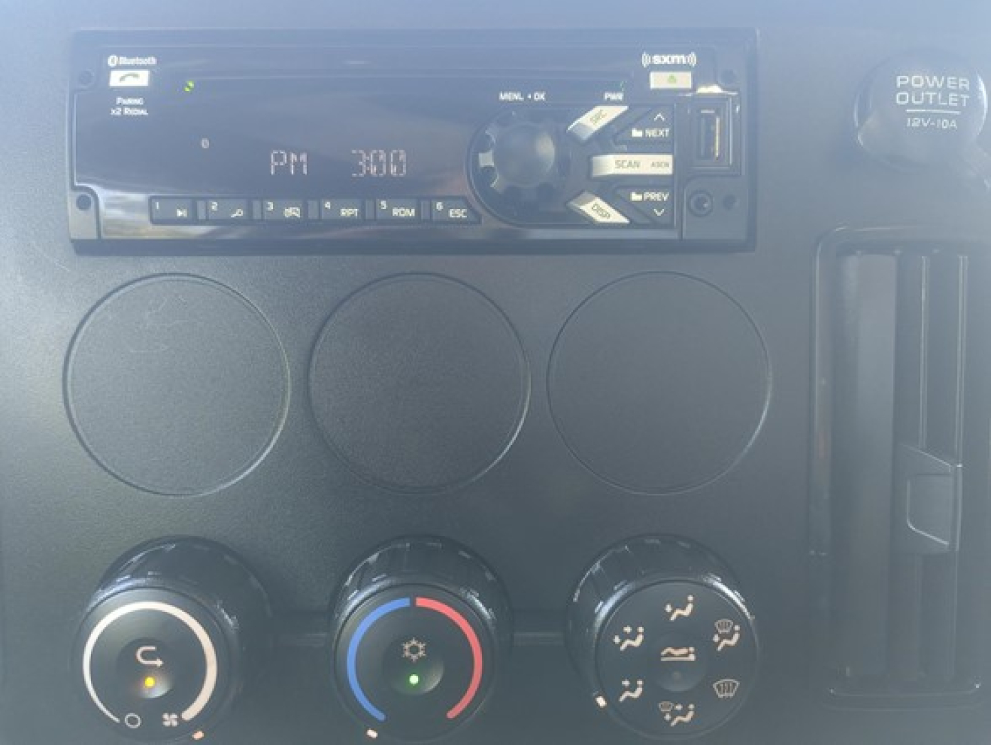 Dashboard area showing a Kenwood-style radio unit with circular climate controls below; three round vents; faint display text on radio; control knobs with blue/red temperature ring.