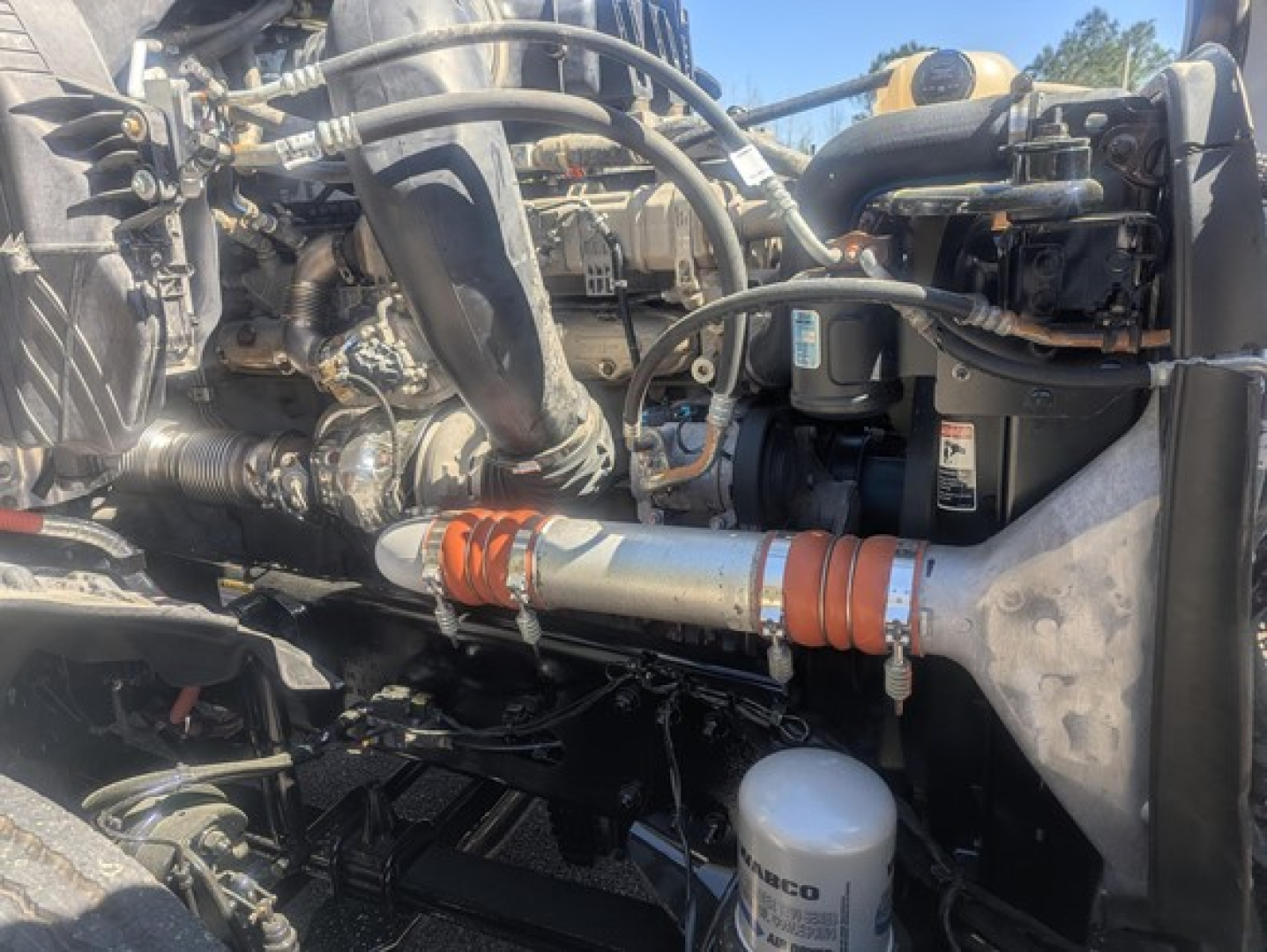 Freightliner Cascadia engine bay showing coolant reservoir, hoses, and metal piping; visible components include air intake hoses and filtration canister.