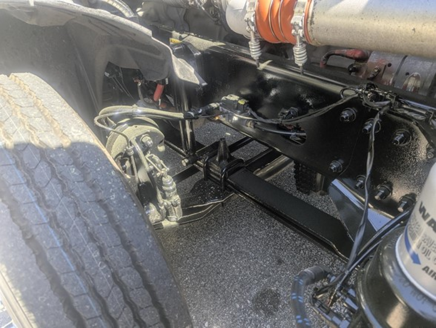 Truck drivetrain undercarriage showing suspension components and axle on Freightliner Cascadia 126, black underframe, tires, hoses, and piping visible