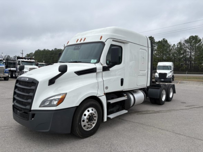 Freightliner Cascadia 126 semi-truck towed in a parking lot, white cab with sleeper, front view showing large grille and side exhaust, no visible sponsor text.