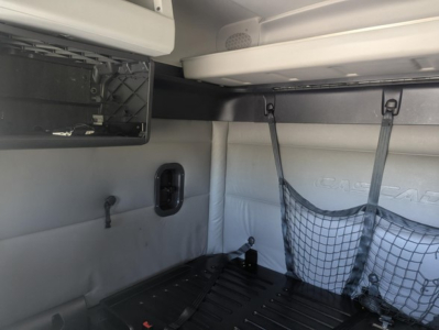 Freightliner Cascadia truck sleeper interior showing storage bin, side wall with net pocket, overhead shelf, and cabin wall with molded logo.