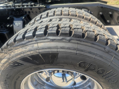 Truck wheel and tire close-up showing heavy-duty dual rear tire with tread pattern and metal rim. Parts of chassis and suspension are visible.