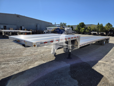 Big Bubba drop deck trailer showing aluminum flatbed with dual rear axles and drop deck in a yard.