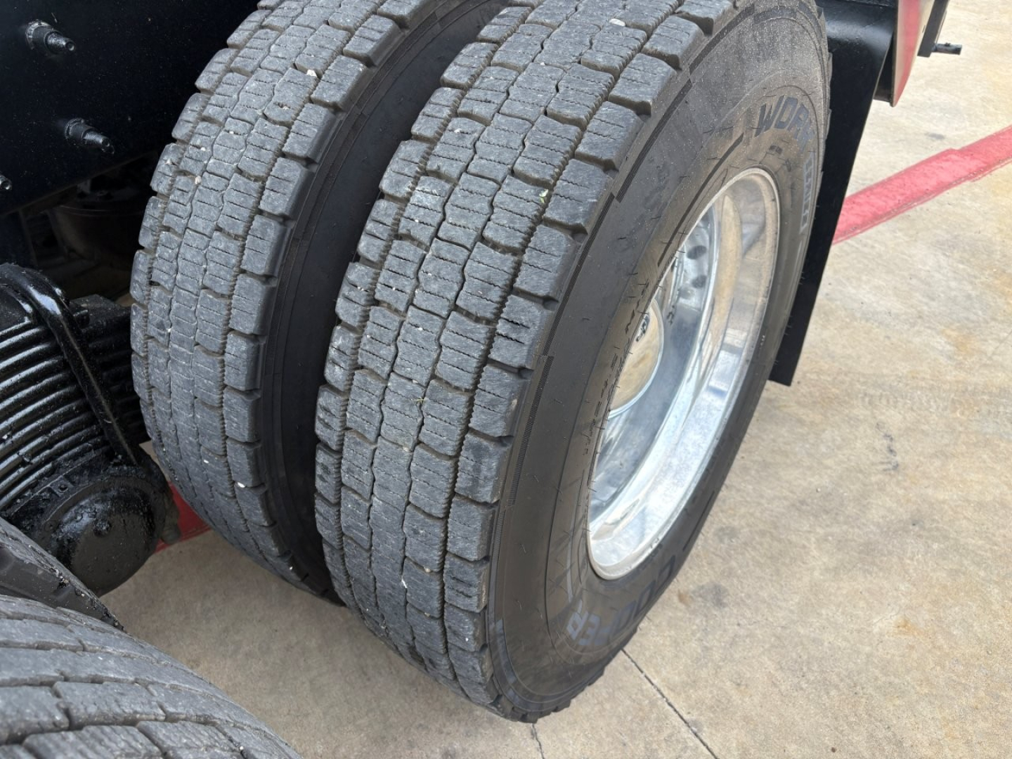 Dual rear wheels on a 2020 Mack GR64F dump truck showing treaded tires and metal wheel, with surrounding concrete surface.