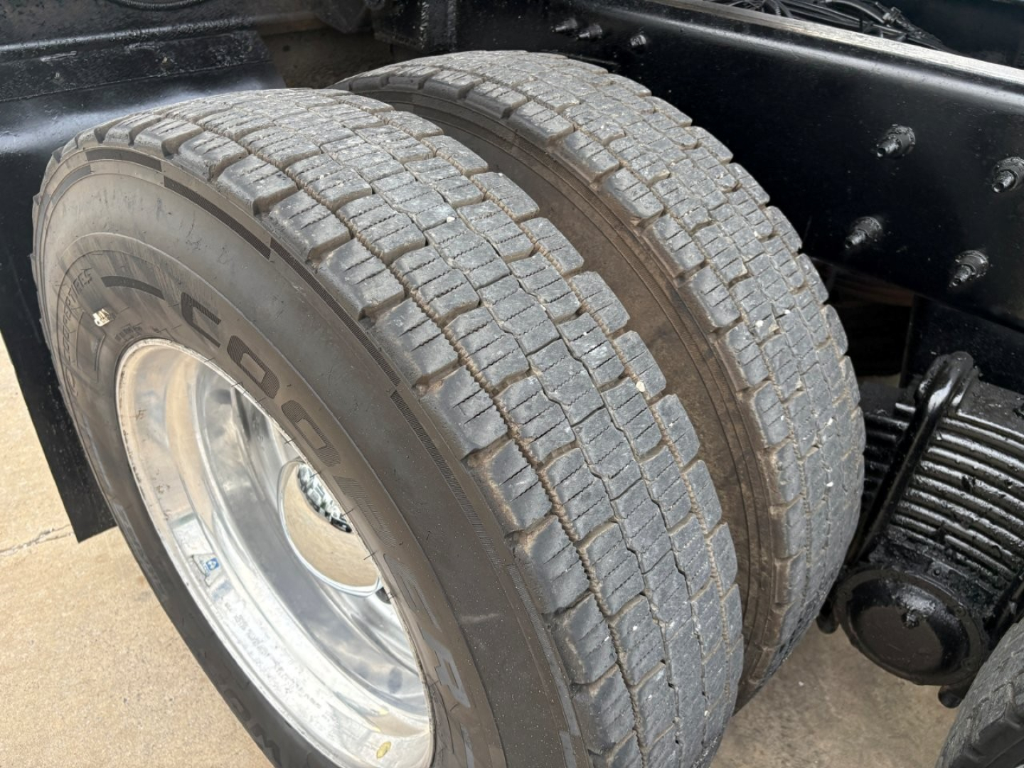 Dual rear steer tires on a Mack GR64F dump truck, showing tread pattern, chrome wheel, and suspension components.