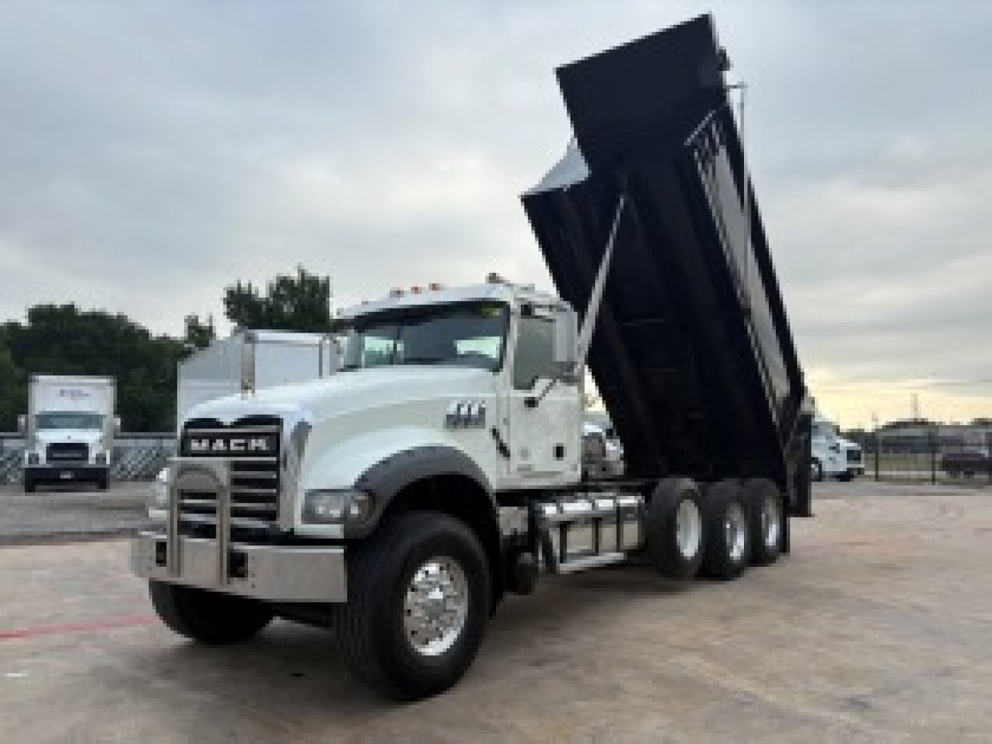 Trucking tractor-trailer in service showing a raised dump bed on a Mack GR64F with white cab and black dump body.