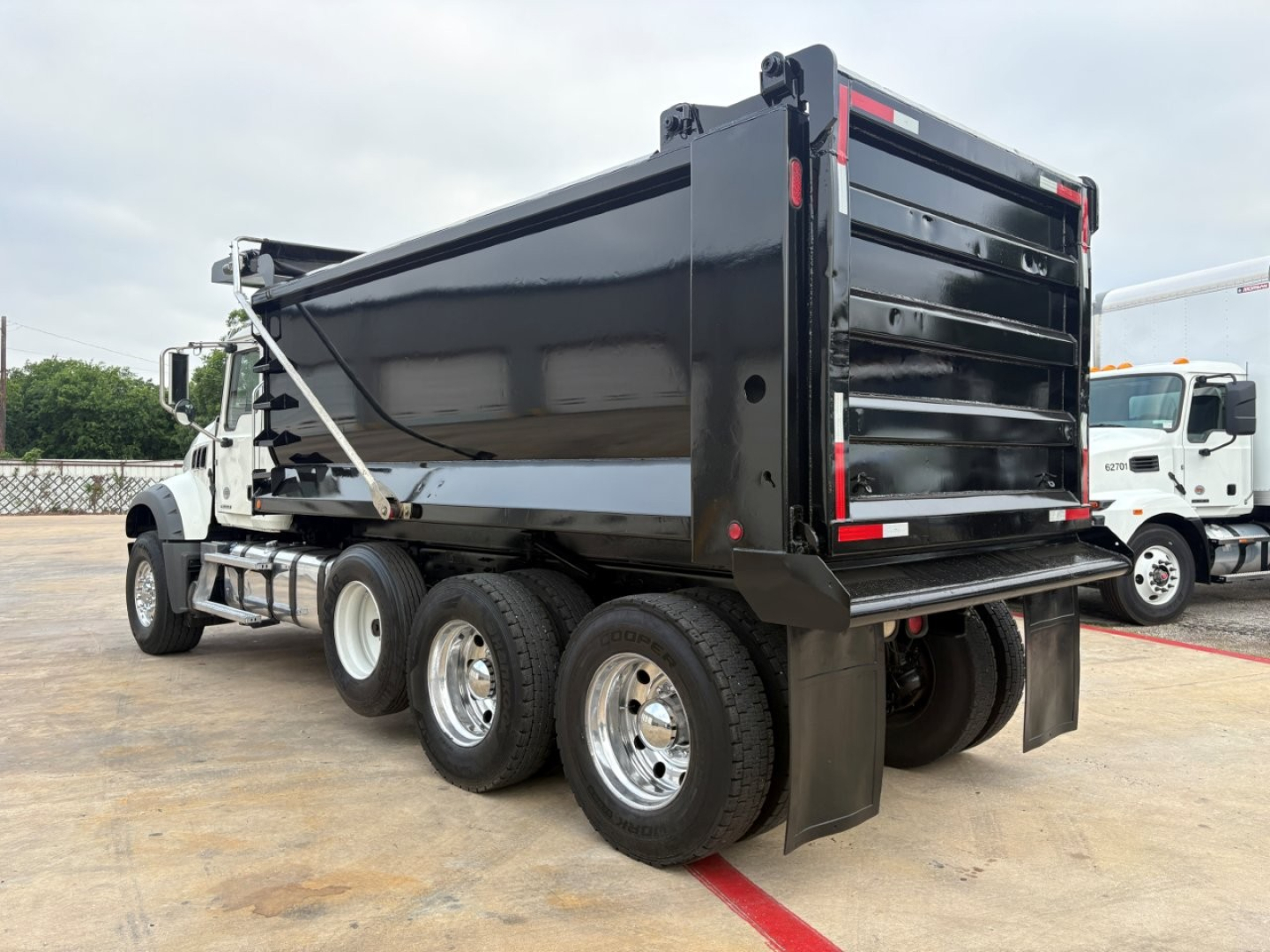 Dump truck rear three-quarter view showing black dump body on Mack GR64F with triple rear axle and white cab. Visible details include dump bed tailgate and taillights.