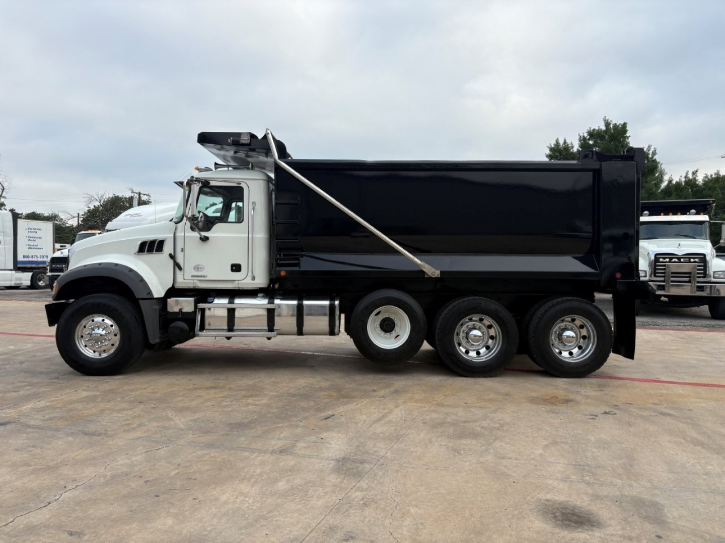 Dump truck side view showing Mack GR64F chassis with black dump body and chrome wheels.