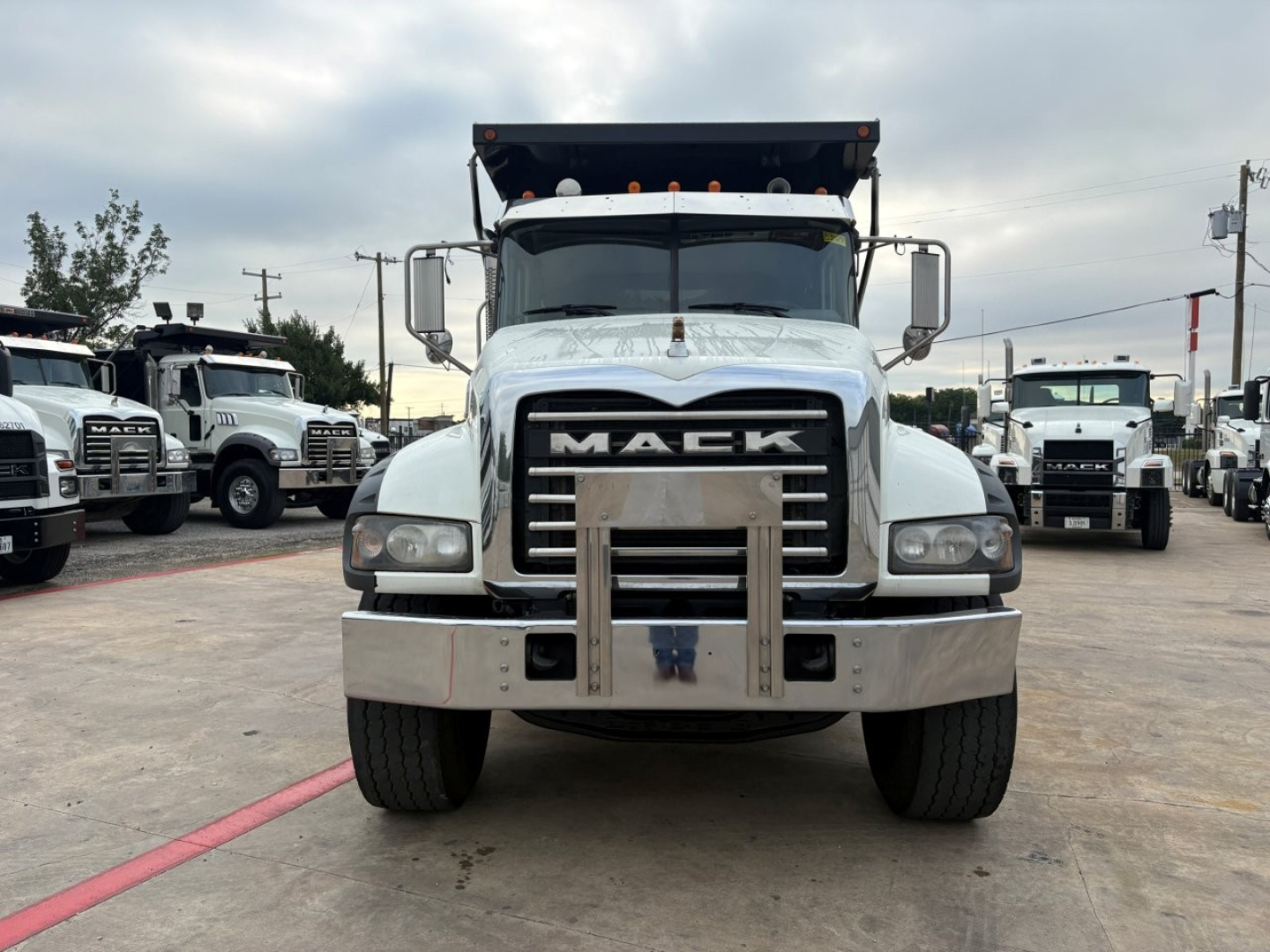 Mack GR64F dump truck front view showing large chrome bumper, grille with MACK emblem, dual headlights, and elevated dump bed in background.