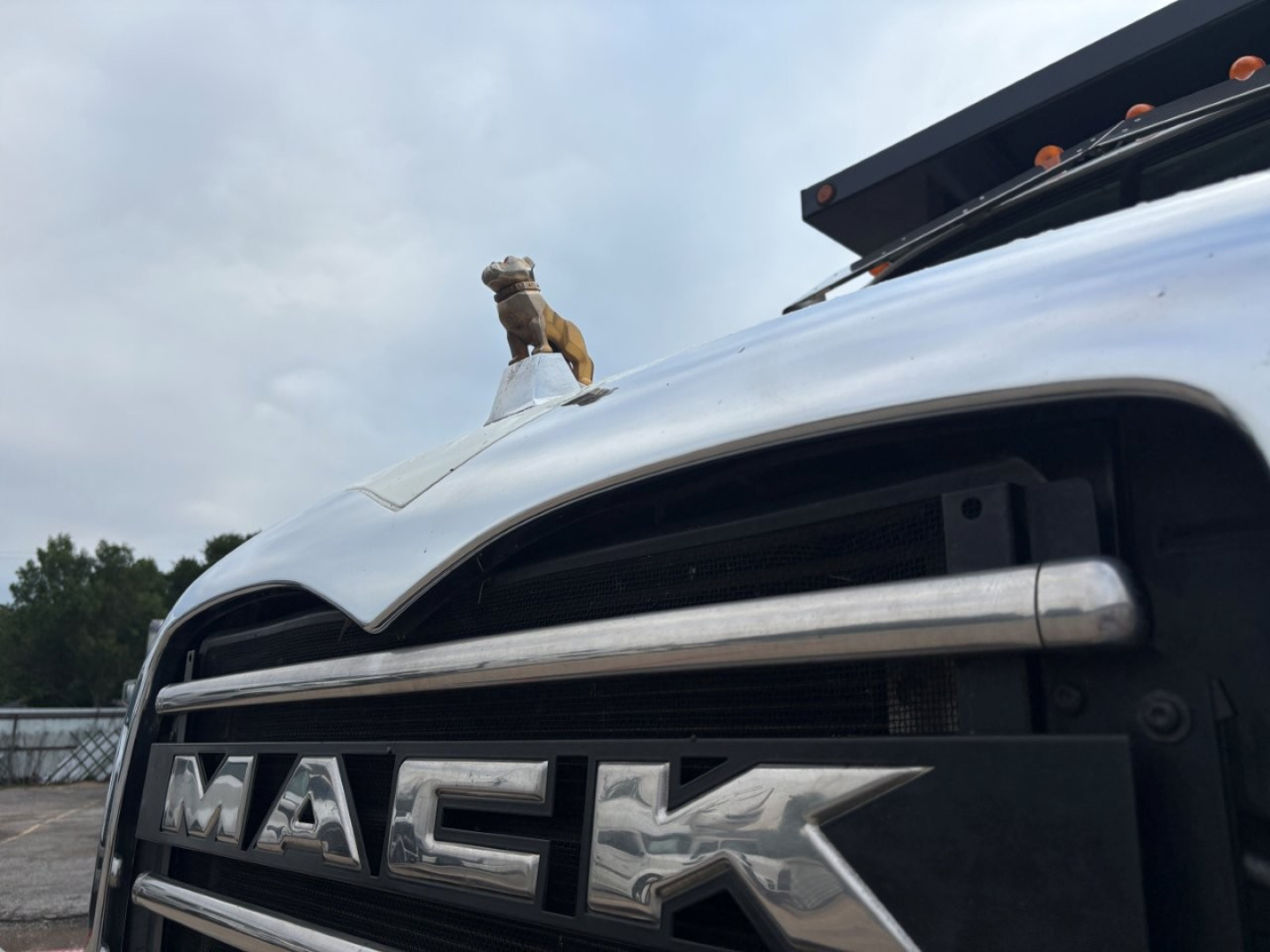 Grille of a 2020 Mack GR64F dump truck showing MACk letters on the grille and hood ornament in the foreground.